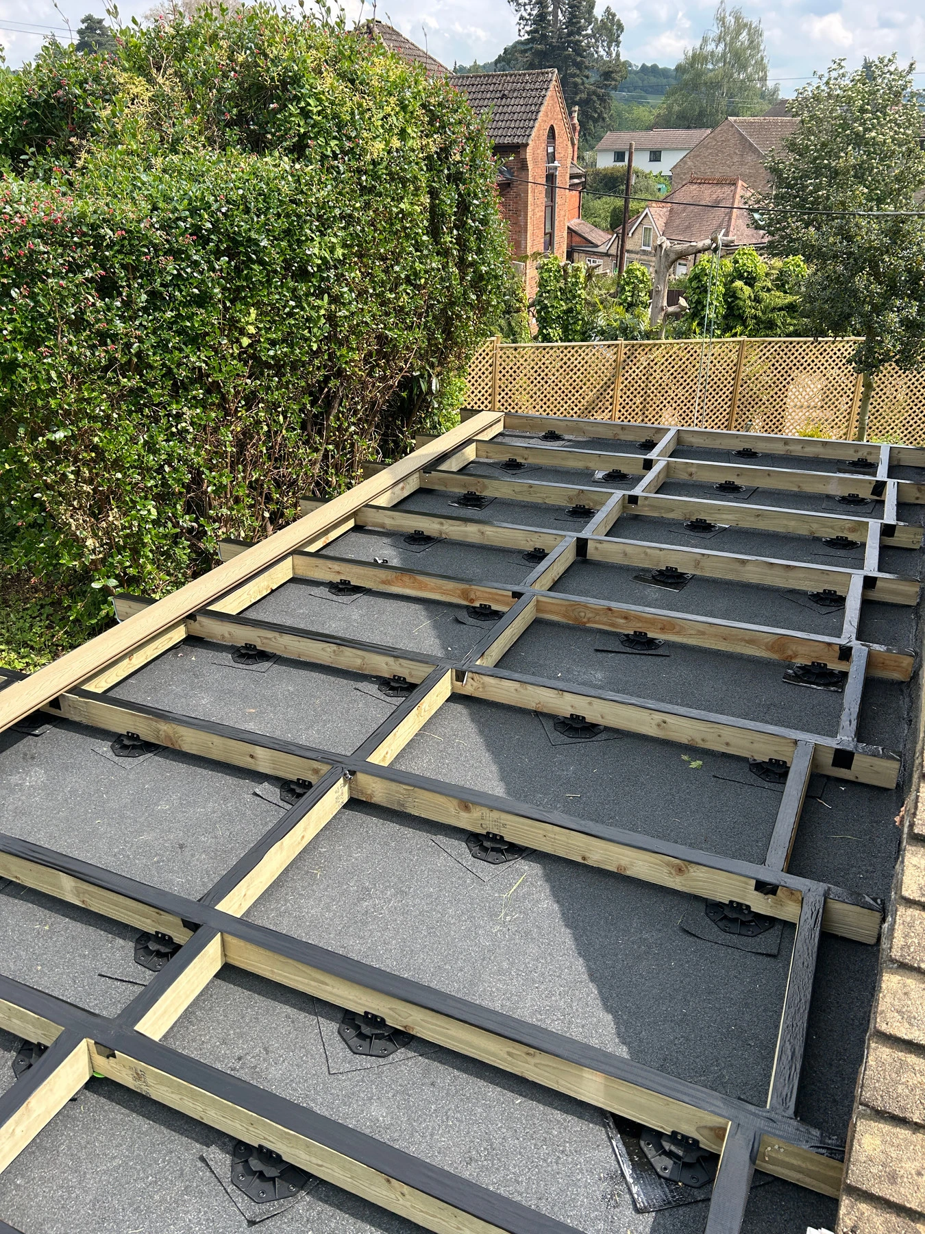Composite decking timber subframe supported on adjustable pedestal system over a flat roof
